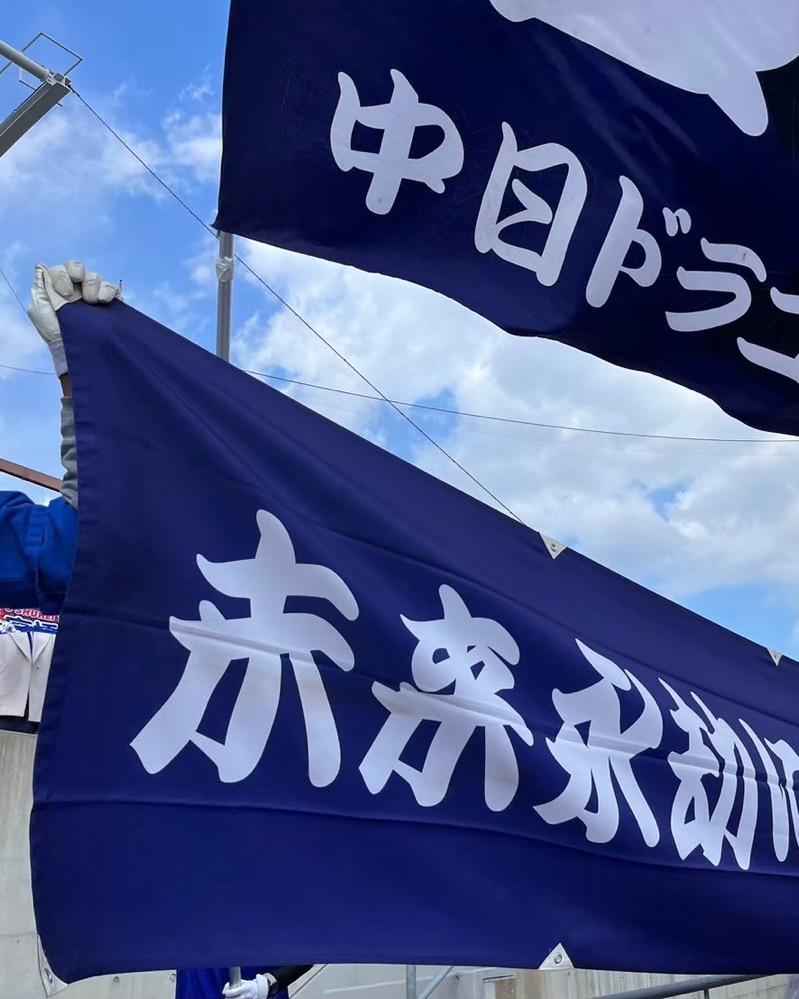 マツダスタジアムで横断幕を掲げる団員の手元と、ひるがえる応援団旗